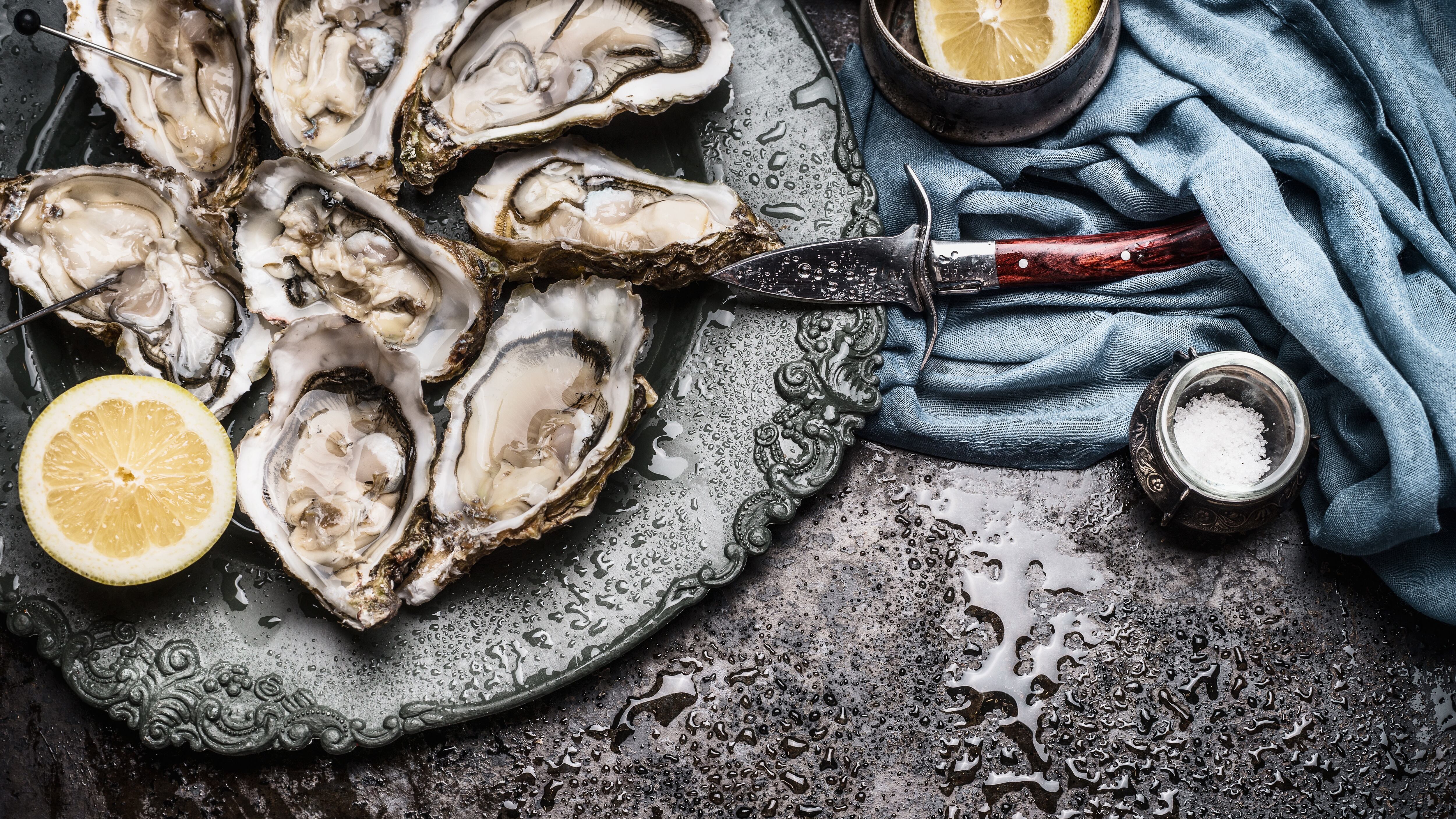 Open wet oysters on a plate with lemon and oysters  knife, dark rustic vintage background, top view, border
